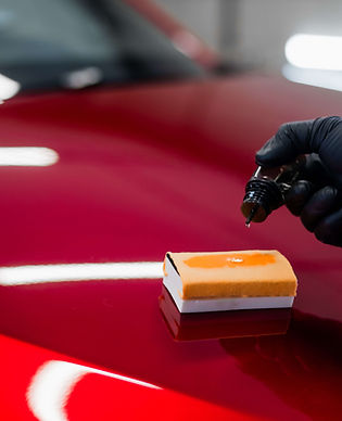 Ceramic coating being applied to a glossy red vehicle panel